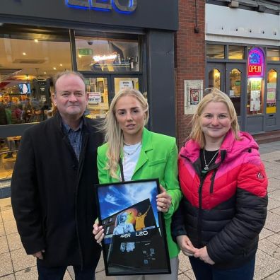 Alex Greenwood (centre) being presented with a framed copy of her mural by Sefton Council Cabinet Members Cllr Ian Moncur (left) and Cllr Trish Hardy (right).